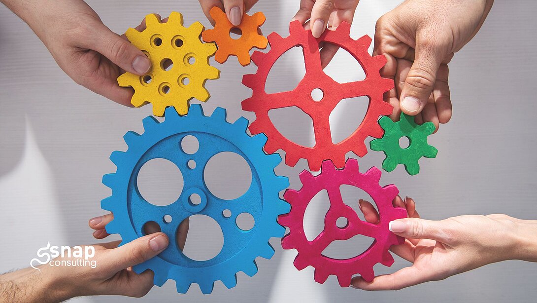Mehrere Hände die bunte verschieden große Zahnräder zusammenhalten. Unten links das snap consulting Logo.