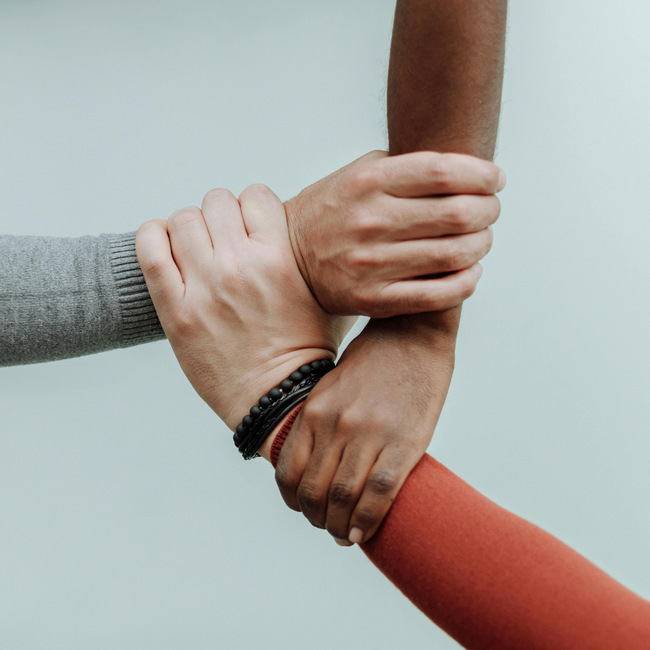 drei Hände die sich gegenseitig am Handgelenk halten.