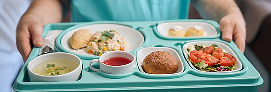 Ein Krankenpfleger serviert Speisen auf einem Tablett.