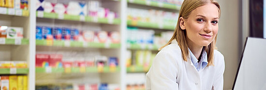 Foto, das eine Apothekerin vor einem Schrank mit Medikamenten zeigt.