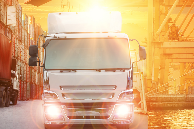 Ein LKW fährt im Sonnenschein mit Scheinwerfern auf die Kamera zu.